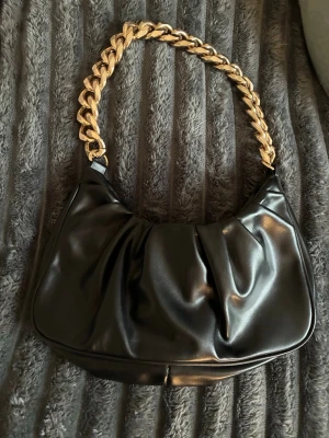 Svart handväska med guldkedja - Trendig svart handväska i glansigt konstläder