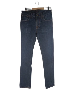 Nudie Jeans Co Grim Tim blå jeans, storlek W32 L34 - Jeans från Nudie Jeans Co. Modellen är Grim Tim och färgen är Dry Navy. Jeansen har knappgylf och fem fickor. Detaljerade sömmar i orange tråd. Midja: 40cm Långt: 79cm