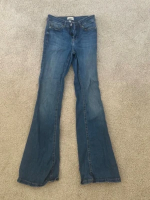 Blå bootcut jeans från ONLY - Säljer ett par klassiska blå bootcut jeans från ONLY. Jeansen har normal midja, fem fickor och dragkedja med knapp. Tillverkade i mjukt denimtyg med lätt slitna detaljer för en avslappnad look.
