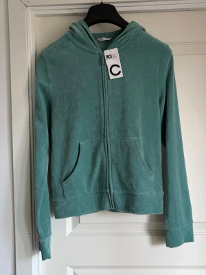 Grön zip hoodie i mjuk frotté - Snygg grön hoodie med dragkedja och huva i mjuk frotté. Har känguruficka framtill och långa ärmar. Perfekt för chill dagar och enkel att matcha med jeans eller mjukisbyxor. Storlek S 