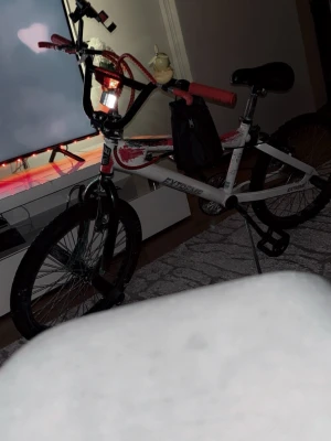 Vit BMX-cykel Extreme - Säljer en vit BMX-cykel från Extreme med svarta och röda detaljer. Cykeln har grova däck, svart sadel och svarta handtag. Ramen är robust och styret är högt, perfekt för tricks och streetriding. Passar dig som vill ha en cool och sportig cykel. Tappade lite färg men är jätte lätt att färga tillbaks det om ni har EX: färg spray. Jätte starka broms och den kan hålla tre personer sedan man kör 