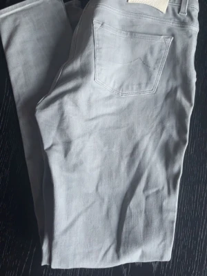 Ljusgrå Jacob Cohen  - Säljer ett par ljusgrå jeans med rak passform och klassiska bakfickor. Jeansen har en enkel design utan synliga loggor och är tillverkade i ett mjukt denimtyg. Perfekta för en clean och stilren look.