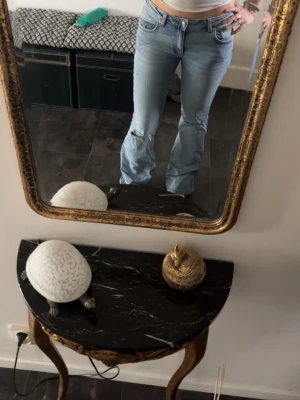 Ljusblå bootcut jeans med slitningar - Säljer ett par ljusblå bootcut jeans med slitningar på knäna. Jeansen har klassisk femficksmodell, normal midja och är i ett mjukt denimtyg. Perfekta för en avslappnad och trendig look.