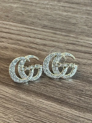 Örhängen - Snygga örhängen i guldton med dubbla G-loggor täckta av glittrande stenar. Helt nya aldrig använda.