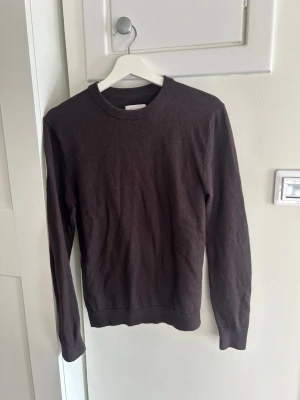 Brun merinoulltröja These Glory Days - Mörkbrun stickad tröja från These Glory Days i mjuk superior merinoull. Klassisk rund halsringning och långa ärmar. Perfekt för dig som gillar stilrena och tidlösa plagg med skön känsla.