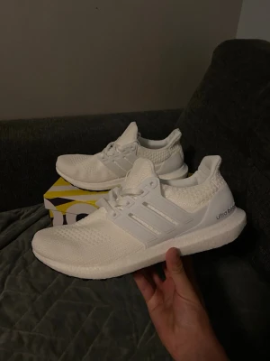Vita Adidas Ultraboost sneakers - Säljer ett par helvita Adidas Ultraboost sneakers med stickad ovandel och klassiska tre ränder på sidan. Skorna har en bekväm och responsiv Boost-sula samt vita snören. Perfekta för dig som gillar stilrena och sportiga sneakers. Skorna är helt nya. Kvitto finns. Hör av er vid funderingar.