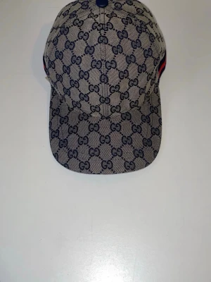 Keps med GG-mönster - Snygg keps i beige canvas med klassiskt mörkblått GG-monogram över hela kepsen. Justerbar rem baktill och blå knapp på toppen. Perfekt accessoar för dig som gillar exklusiv streetstyle.