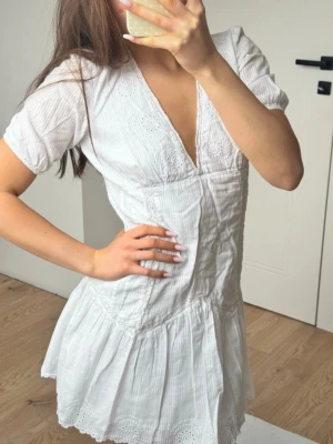  Ny slutsåld Vit kort  student klänning med spetsdetaljer från Zara  - Söt vit kortklänning med v-ringning och broderade spetsdetaljer. Klänningen har korta ärmar, lätt rynkad kjol och tunna vertikala ränder i tyget. Perfekt för sommarens alla tillfällen.