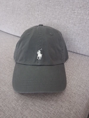 Svart keps från Polo Ralph Lauren - Snygg svart keps från Polo Ralph Lauren med den klassiska broderade loggan i vitt framtill. Kepsen har böjd skärm och justerbar rem bak. Tillverkad i bomull för en bekväm och stilren look.