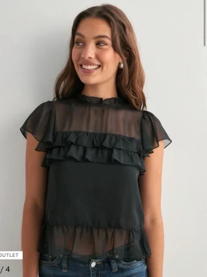 Svart volangblus ifrån nelly - VÅGA SÄTT PRISFÖRSLAG !!!Trendig svart blus i transparent material med volangdetaljer över bröstet och vid fållen. Blusen har korta ärmar och hög halsringning. Perfekt att styla med jeans eller kjol för en cool look.