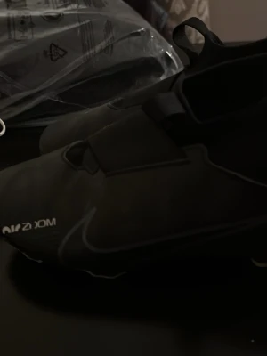 Nike Mercurial svarta fotbollsskor - Säljer ett par svarta Nike Mercurial fotbollsskor med stilren design och diskret Nike-logga. Skorna har en strumpliknande passform och täckt snörning för bättre bollkontroll. Perfekta för dig som vill ha grym touch och snabbhet på planen.