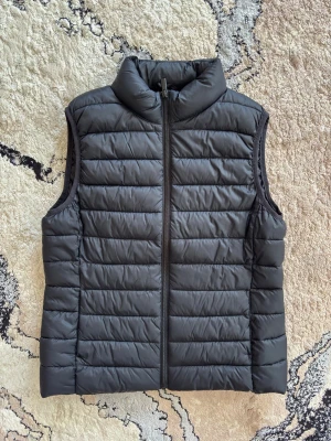 Svart dunväst  - Snygg svart dunväst som funkar perfekt för både våren och sommaren. Västen har en stilren design med dragkedja framtill och är tillverkad i ett lätt, vadderat material som håller värmen. Perfekt att slänga över en hoodie eller tröja för extra värme. Anledning till att jag säljer är på grund av att jag gillar inte väst.
