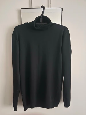 Tröja  - Klassisk svart stickad polotröja från Viole med hög krage och långa ärmar. Tröjan har en enkel och stilren design, perfekt att matcha med olika outfits. Materialet är mjukt och bekvämt, och kragen är ribbstickad för extra komfort.