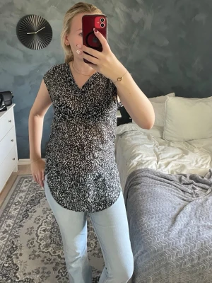 Svartvit mönstrad topp  - Säljer en svartvit mönstrad topp. Toppen har v-ringning, är ärmlös och har en längre, rundad nederkant. Perfekt till jeans eller kjol. 