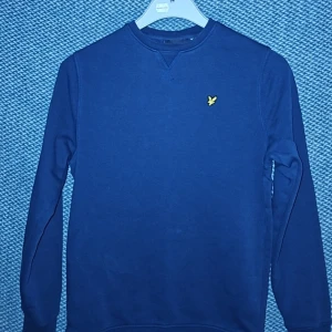 Blå sweatshirt från Lyle & Scott - Mörkblå sweatshirt från Lyle & Scott med klassisk rund halsringning och den ikoniska gula örnloggan broderad på bröstet. Tröjan har långa ärmar och ribbade muddar vid ärmslut och nederkant. Perfekt för en avslappnad och stilren look. Är öppen för prisförslag vid snabb försäljning.