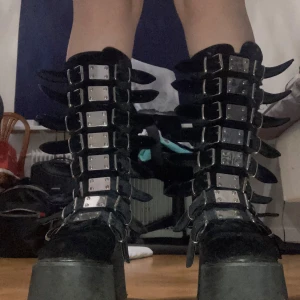 Svarta Demonia plattform boots stl 42 - Säljer ett par svarta Demonia damned 318 boots med rejäl plattformssula och knähög passform, med tygmaterial black velvet. Jag fick dessa skor av en gammal kompis som var originalägaren. Skorna har använts flitigt, med ordentligt slitage på hälarna och det är därför jag säljer de för ca 1/3 av originalpriset som då ligger på 1900 kr hos Demonia. Har dock ej kvar originallådan så kommer att använda en annan kartong. Hör av er vid frågor!