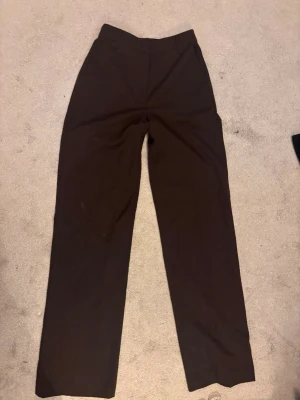 Bruna kostymbyxor med raka ben - Snygga bruna kostymbyxor med hög midja och raka ben. Klassisk design utan synliga fickor eller detaljer, perfekta för en stilren look. 