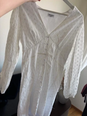 Vit studentklänning  - Superfin vit kort klänning från bubbleroom i storlek M med broderade blommor, v-ringning och knappar framtill. Klänningen har långa ärmar och är gjord i bomull, perfekt för sommarens alla tillfällen. Endast använd en gång. I nyskick 