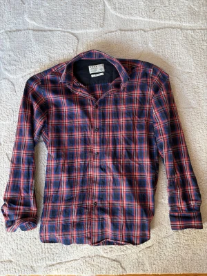 Rutig skjorta från Jack & Jones - Snygg långärmad skjorta från Jack & Jones i rött, blått och vitt rutmönster. Skjortan har klassisk krage, knappar framtill och är tillverkad i mjuk bomull. Perfekt för en avslappnad men stilren look.