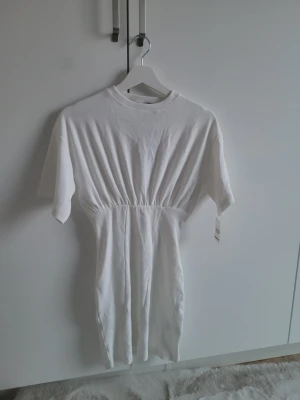 Miniklönning - Vit kortklänning från Boohoo med rund halsringning och korta ärmar. Klänningen har en markerad midja och är tillverkad i ett mjukt bomullsmaterial. Enkel och stilren design som passar perfekt till sommaren.