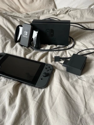 Nintendo Switch med tillbehör - Säljer en svart Nintendo Switch med Joy-Con-kontroller, nästan helt oanvänt därmed bra skick. Man kan koppla upp på tvn eller spela på den Lill skärmen 