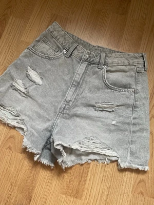 Gråa high waist jeansshorts Divided - Säljer ett par gråa högmidjade jeansshorts från H&M Divided. Shortsen har slitna detaljer, råa kanter och klassisk femficksdesign. Perfekta för sommaren och ger en avslappnad vibe. Den har en liten fläck som ni ser på sista bilden😊