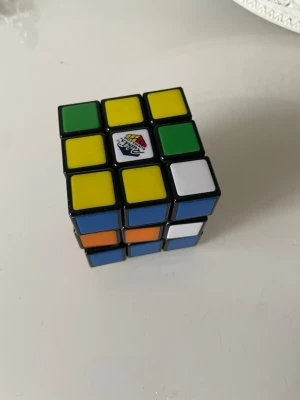 Rubiks kub  klassisk färgglad - Klassisk Rubiks kub  med färgerna gul, grön, blå, vit, orange och röd. Kuben har svart plast som bas och färgade klistermärken på varje sida. Perfekt för dig som gillar kluriga pussel och vill utmana hjärnan.