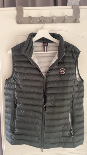 Grön dunväst från Colmar - Snygg grön dunväst från Colmar med quiltad design och dragkedja framtill. Västen har två praktiska fickor med dragkedja och en hög krage. Insidan är ljusgrå och materialet är lätt och smidigt, perfekt för lager på lager under kyliga dagar.