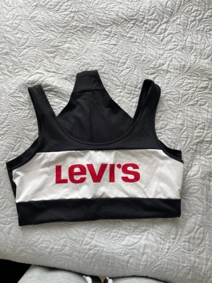 Svart och vit baddräkt från Levi's -  baddräkt från Levi's i svart och vitt med axelband och klassisk rund halsringning. Framtill finns en vit panel med Levi's-loggan i rött. Materialet är stretchigt och bekvämt, perfekt för strand eller pool. Snygg och sportig design. Den är använd men fortfarande i bra skick. 