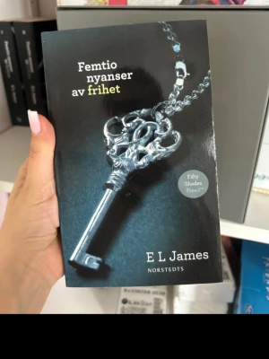 Femtio nyanser av frihet bok - En svensk pocketbok av E L James med titeln 'Femtio nyanser av frihet'. Omslaget är svart med en silverfärgad nyckel i kedja. Boken ges ut av Norstedts och är en del av Fifty Shades-serien.