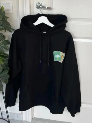 Drole de Monsieur – Hoodie - Säljer en drole de monsieur svart hoodie med huva och dragsnören. På bröstet och ryggen finns tryck av spelkort i grönt och vitt, där ett av korten har texten 'OROLE'. Hoodien har en avslappnad passform och är perfekt för dig som gillar streetwear och unika detaljer.