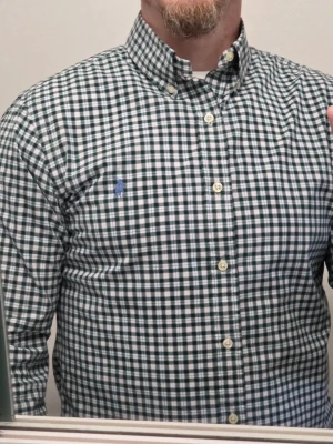 Ralph Lauren polo  - Snygg grön och vit rutig skjorta med klassisk button-down krage och långa ärmar. Skjortan har knappar framtill och en liten broderad logga på bröstet. Perfekt för dig som gillar en stilren och tidlös look. Slim Fit stretch.