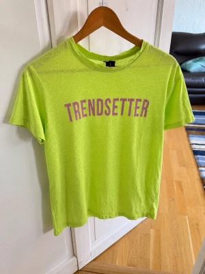 Limegrön T-shirt från Bershka - Trendig limegrön T-shirt från Bershka med lila texten 'TRENDSETTER' framtill. Modellen är croppad med korta ärmar och rund halsringning. Perfekt för dig som vill sticka ut med färg och stil.