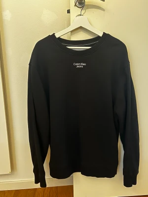 Svart sweatshirt från Calvin Klein  - Säljer en svart sweatshirt från Calvin Klein Jeans med diskret logga broderad på bröstet. Tröjan har rund halsringning, långa ärmar och ribbade muddar vid ärmslut och nederkant. Perfekt för en clean och stilren look. Använd 2-3 gånger. 