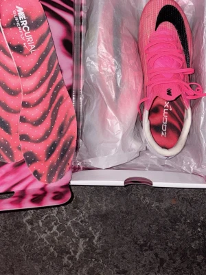 Nike Mercurial rosa fotbollsskor - Säljer ett par Nike Mercurial Superfly fotbollsskor i en riktigt snygg rosa färg med svart swoosh och vita detaljer. Skorna har en modern, strömlinjeformad design och kommer med matchande innersulor med mönster. Perfekta för dig som vill sticka ut på planen.