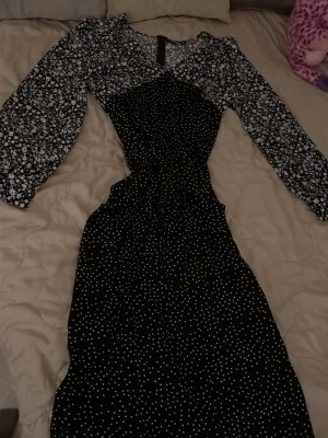 Svart blommig och prickig klänning Missguided - Snygg svart klänning från Missguided med vita blommor på ärmarna och prickigt mönster på resten av klänningen. Långärmad modell med markerad midja och figurnära passform. Perfekt för dig som gillar kontraster och trendiga detaljer.