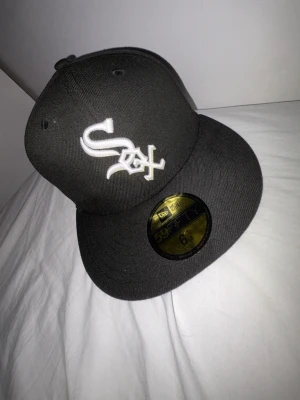 Svart New Era White Sox keps - Säljer en svart New Era 59FIFTY keps med White Sox-logga broderad i vitt framtill. Klassisk flat brim och broderad New Era-logga på sidan. Tillverkad i ett slitstarkt tyg som ger en clean och sportig look.