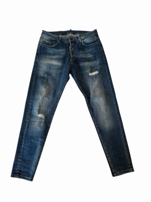 Blå slitna jeans från Dsquared2 - Säljer ett par blå jeans från Dsquared2 med slitningar och distressed detaljer på både fram- och baksida. Jeansen har smal passform, klassisk femficksmodell och tryck på ena bakfickan. Materialet är denim i bomull med en cool tvätt.