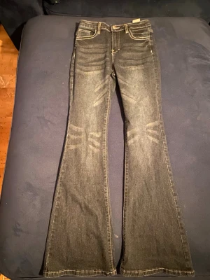 Mörkblå bootcut jeans med detaljer - Snygga mörkblå bootcut jeans med slitningar framtill och kontrastsömmar. Jeansen har dekorativa fickor bak med knappar och mönstrade detaljer. Klassisk femficksmodell i stretchigt denimtyg som ger en bekväm passform.
