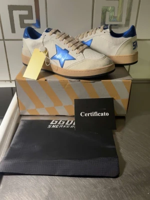 GGDB Ballstar sneakers med blå stjärna - Snygga GGDB Ballstar sneakers i vitt läder med beige mockadetaljer och en metallicblå stjärna på sidan. Skorna har blå hälkappa, beige sula och vita skosnören. Perfekt för dig som vill sticka ut med en unik och trendig sneaker.