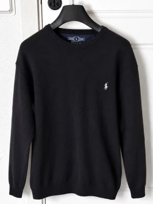 Svart stickad tröja från Polo Ralph Lauren - Klassisk svart stickad tröja från Polo Ralph Lauren med rund halsringning och den ikoniska broderade loggan i vitt på bröstet. Tröjan har ribbade muddar vid ärmslut och nederkant, vilket ger en snygg och stilren look. Perfekt att matcha med jeans eller chinos.