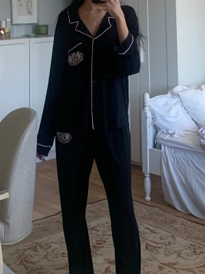 Svart pyjamas med rosa detaljer Juice couture  - Snygg svart pyjamas med rosa kontrastsömmar och emblem på bröstficka och byxficka. Setet består av långärmad skjorta med krage och matchande byxor. Perfekt för mysiga kvällar hemma.