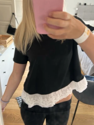 Svart topp med spetsdetalj - Snygg svart topp med korta ärmar och rund hals. Nedtill har toppen en bred vit spetskant som ger en romantisk touch. Perfekt att styla med jeans eller kjol för en trendig look.