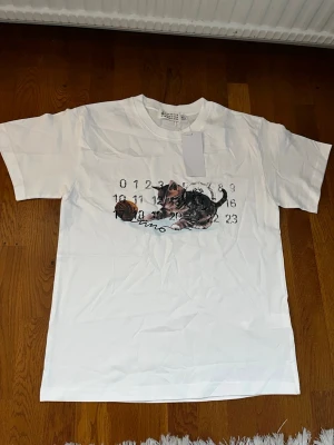 Maison Margiela T-Shirt Vit Katt, S - Säljer denna t-shirt i storlek S, men skulle säga att den är stor i storleken och passar perfekt även för en M! 