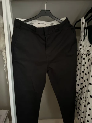 Svarta chinos från Dickies - Snygga svarta chinos från Dickies med klassisk rak passform och diskreta sidofickor. Tillverkade i ett slitstarkt bomullsmaterial som ger en clean och stilren look. Perfekta för dig som gillar streetwear och enkel stil.