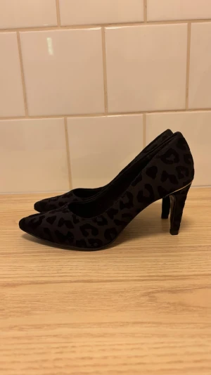Svarta pumps med leopardmönster - Snygga svarta pumps från Tamaris med leopardmönster i sammet. Skorna har spetsig tå och smal klack som ger en elegant siluett. Materialet är mjukt och ger en lyxig känsla. Perfekta för dig som vill sticka ut med ett djurmönster. Inte använda endast provade. Tror inte just dessa finns lägre ute på marknaden.