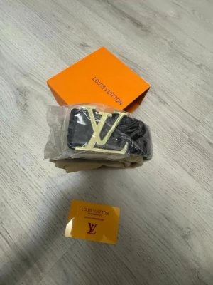 Svart bälte med gulddetalj - Snyggt svart bälte  med stor guldfärgad logga som spänne. Bältet har en klassisk design och kommer i originalförpackning med tillhörande dustbag och kort. Perfekt accessoar för att lyfta din outfit.