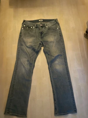True Religion ljusblå bootcut-jeans – fint skick - Säljer ett par äkta True Religion-jeans i ljusblå tvätt. Bootcut-modell med de klassiska bakfickorna. Jeansen är i fint begagnat skick med normalt slitage och inga hål eller större fläckar.