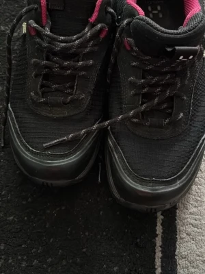 Svarta sneakers från Haglöfs Vision GT - Säljer ett par svarta Haglöfs Vision GT sneakers med rosa detaljer och snörning. Ovandelen är i syntetfiber och syntetläder, sulan är i gummi. Skorna har en sportig look och passar perfekt för dig som gillar stilrena sneakers.