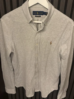Ljusgrå skjorta från Ralph Lauren - Klassisk ljusgrå skjorta från Ralph Lauren med knappslå och broderad logga på bröstet. Väldigt skön tyvärr blivit för liten.